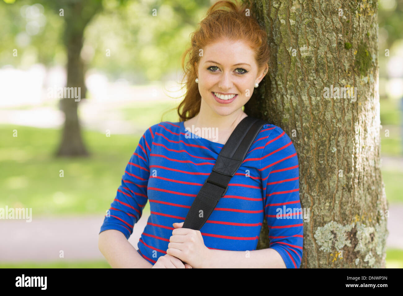 Smiling pretty redhead leaning against a tree Stock Photo
