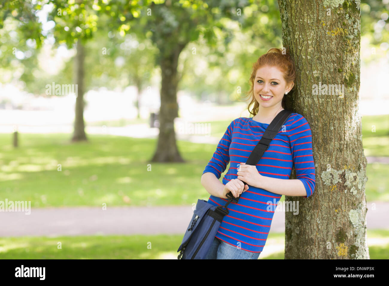 Smiling redhead student leaning against a tree Stock Photo