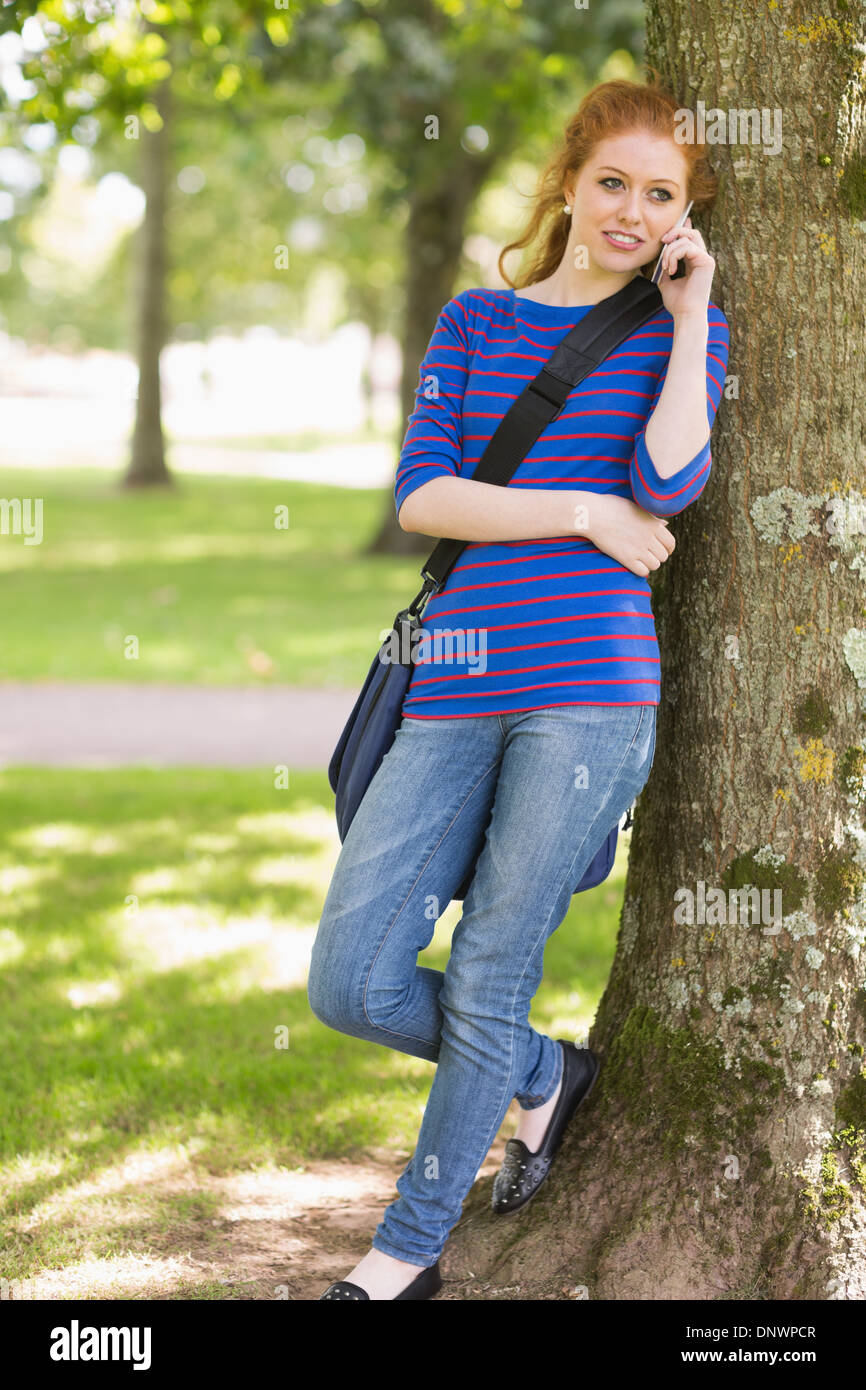Redhead student leaning against a tree talking on the phone Stock Photo