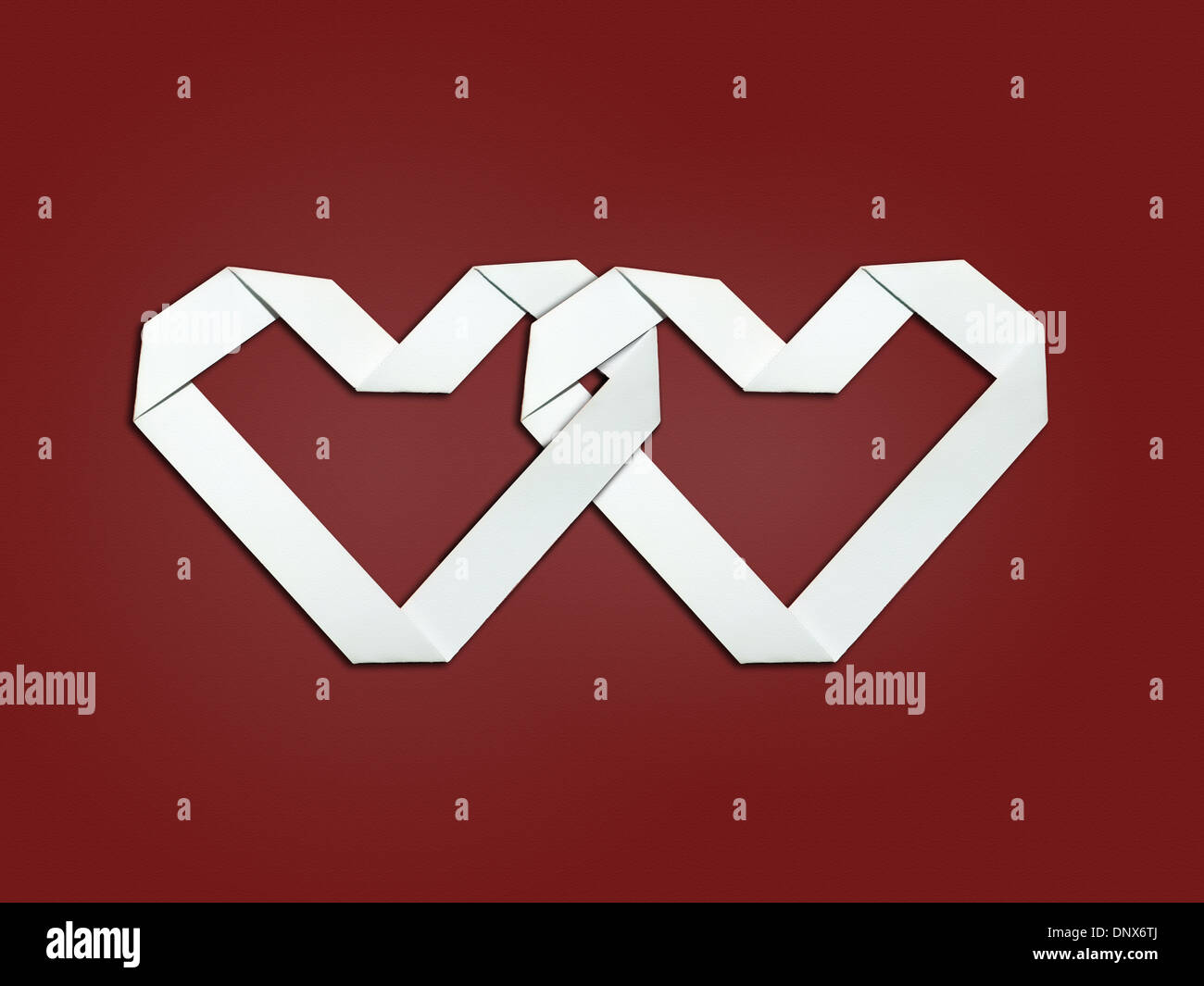 Two overlapping hearts made from white paper on red background - Valentine concept Stock Photo