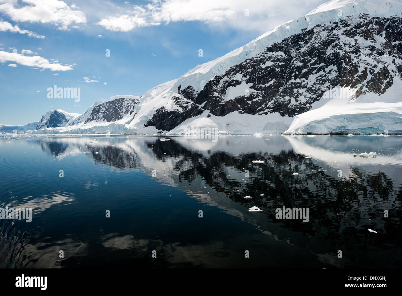 Neko Harbour Mountains And Reflections Antarctica // NEKO HARBOUR, Antarctica—The icy and rocky scenic landscape mountains covered in ice and snow at Neko Harbour on the Antarctic Peninsula is reflected on glassy mirror-like calm waters. Stock Photo