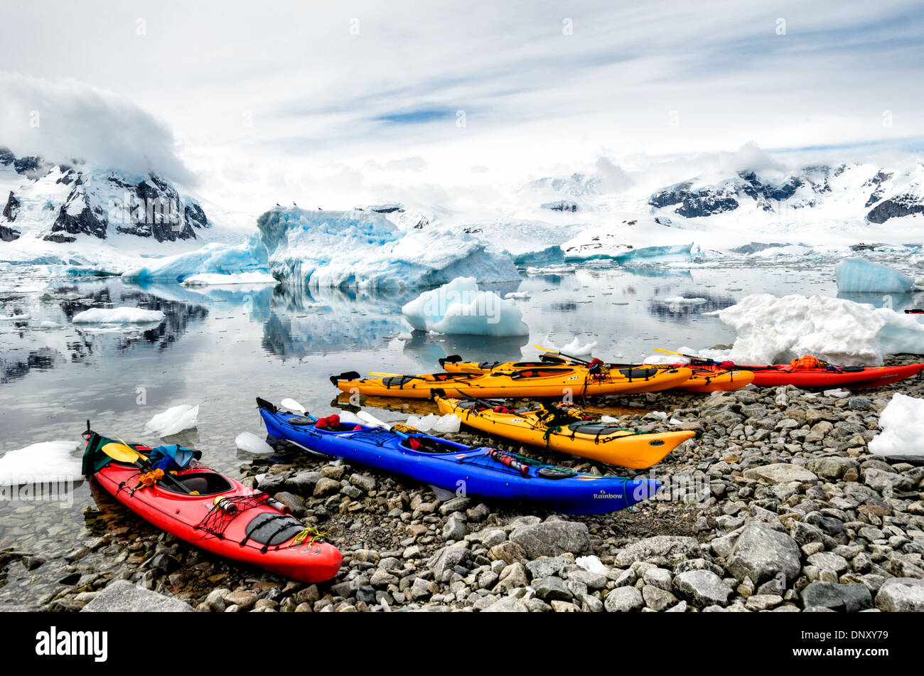 CUVERVILLE ISLAND, Antarctica — A group of brightly colored kayaks rests on the rocky shore of Cuverville Island on the Antarctic Peninsula. The vibrant vessels contrast sharply with the stark, monochromatic landscape, creating a vivid scene that captures the intersection of adventure tourism and the pristine Antarctic environment. Stock Photo