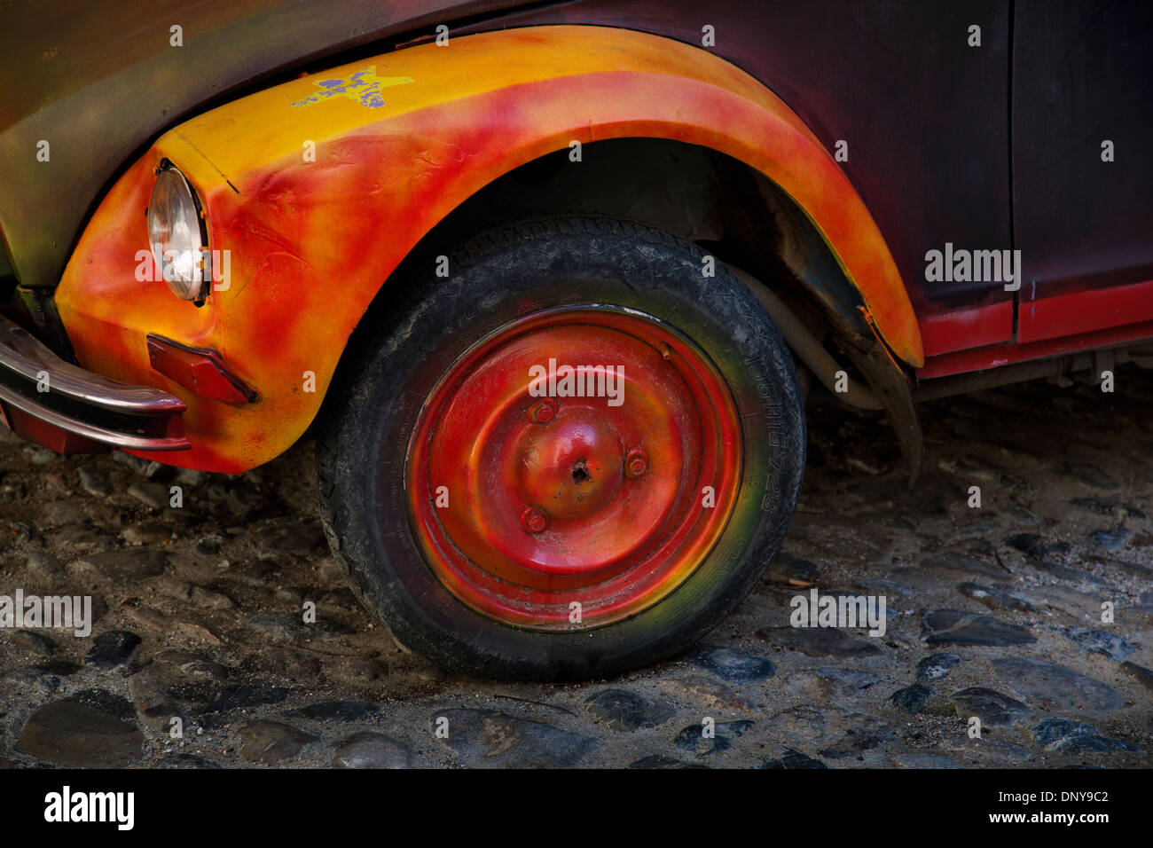 Brightly painted orange & yellow 2CV French car wheel on cobbled street, France Stock Photo