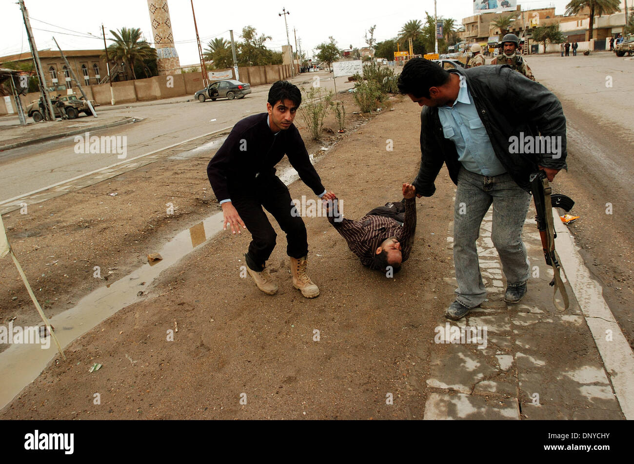 Jan 26, 2006; Abu Ghraib, Baghdad, IRAQ; Iraqi police drag the wounded insurgent away from his smashed up car in Baghdad on Jan. 26, 2006. The insurgent was shot 20 times during a gun battle between American soldiers and a car of four insurgents. Iraqi Ministry of Defense identification cards and drug-filled syringes were found in the car along with four AK-47s, one PKM machine gun Stock Photo