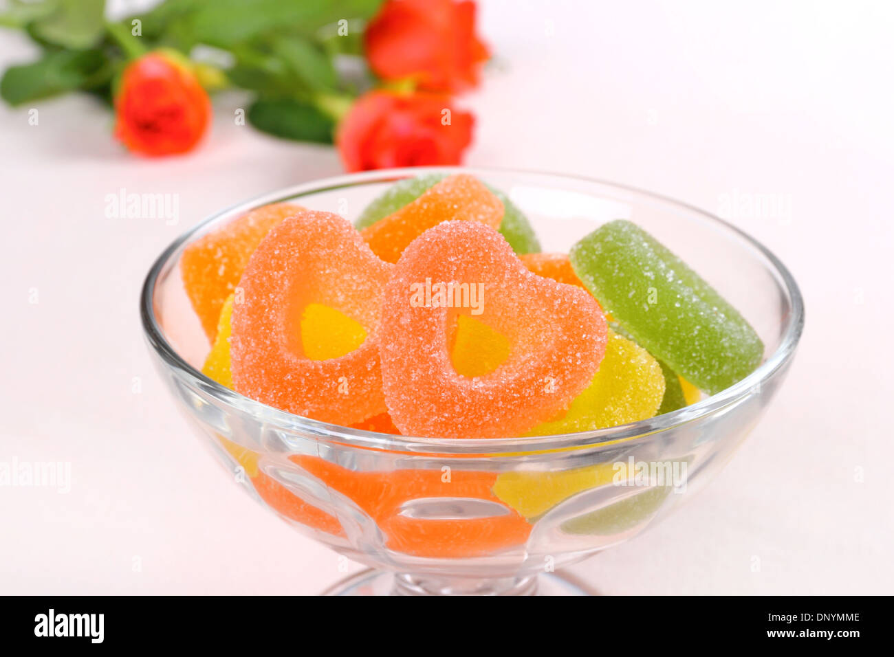 Colored candies with two red hearts in glass bowl and roses, close up Stock Photo