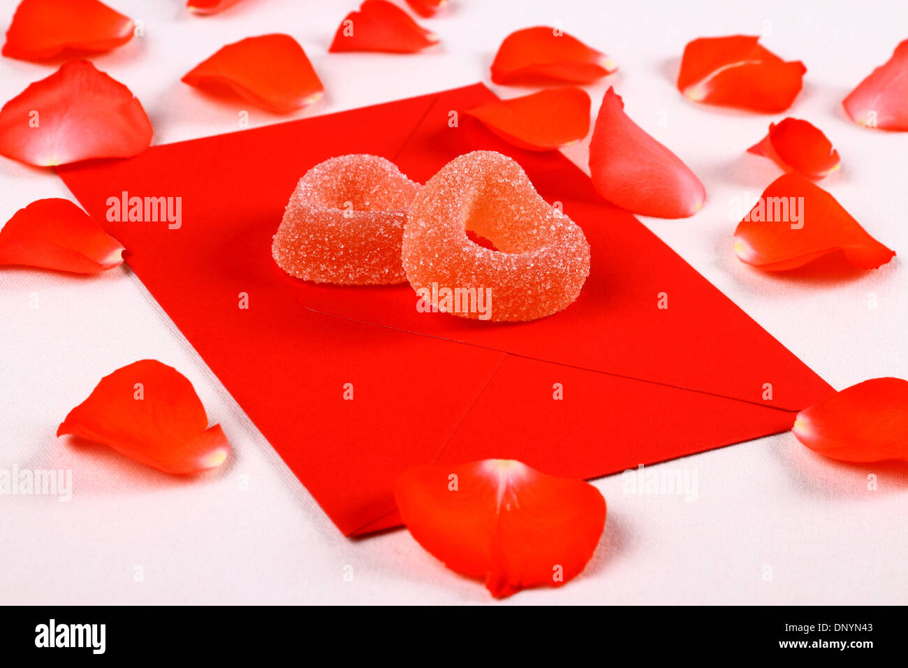 Two hearts from sugar candies on red envelope and petals, close up Stock Photo