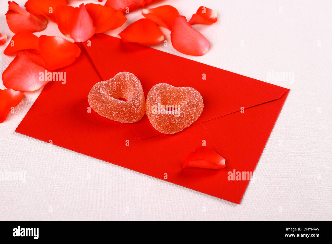 Two hearts from sugar candies on red envelope and petals, close up Stock Photo