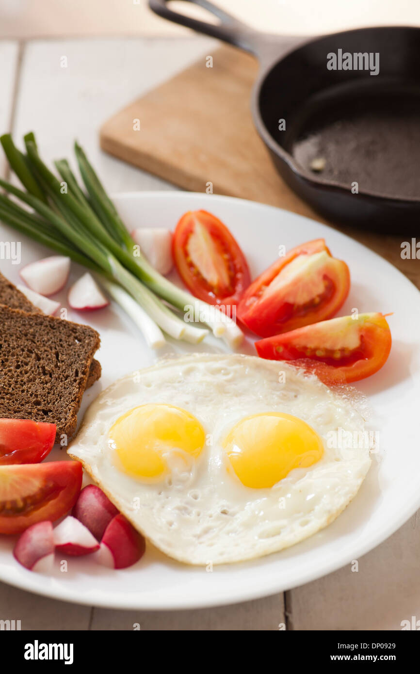 Two fried eggs with yellow yolks and vegetables Stock Photo