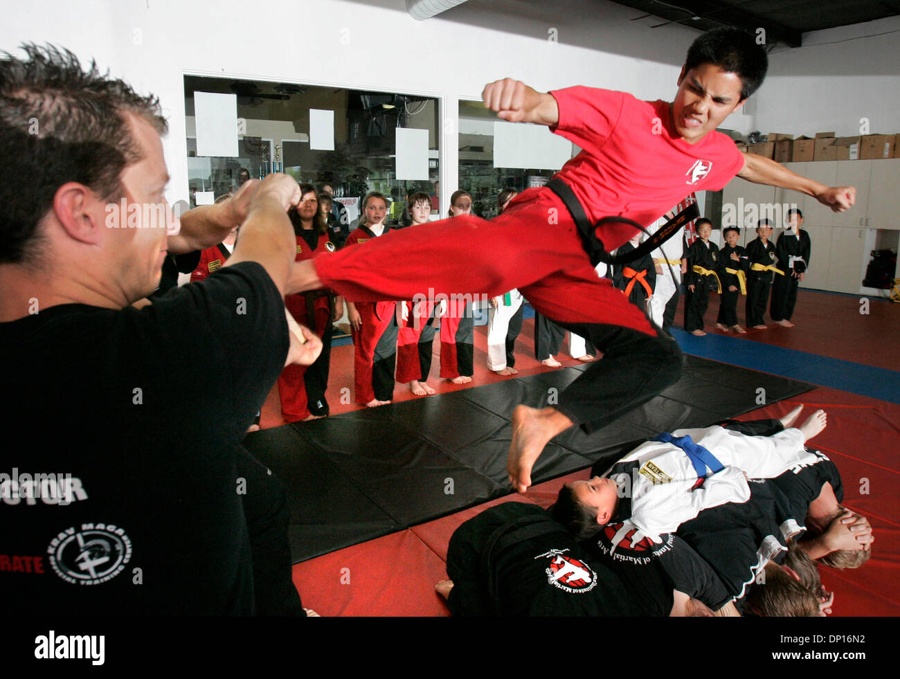 Apr 21, 2006; San Marcos, CA, USA; At the International Institute of Martial Arts instructor STEVEN NGUYEN performs a flying side kick to break a board held by Chief Instructor TRAVIS BARTLETT, at close left, as he leaps over young student PARKER RUTHERFURD that's laying on top of other students. They're practicing for their upcoming demonstration. Mandatory Credit: Photo by Charli Stock Photo