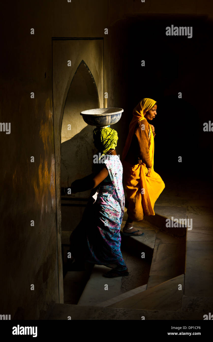 Two women passing by the opposite direction an arch way in Jaipur, India. One carrying a bowl. Great light, moment and colors. - Stock Image