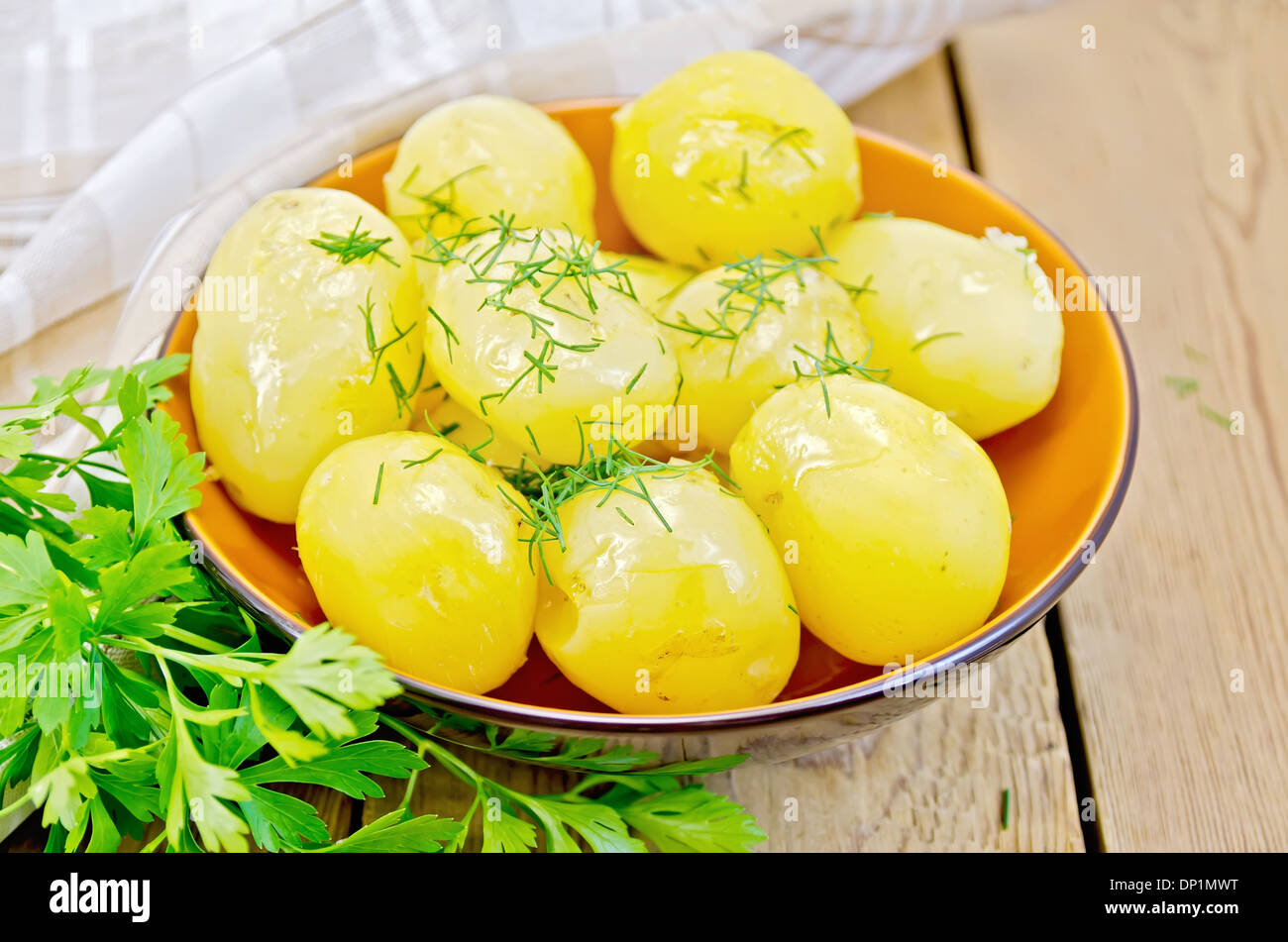 Boiled potatoes with dill, butter drizzled in pottery, a bunch of parsley, a napkin on wooden board Stock Photo
