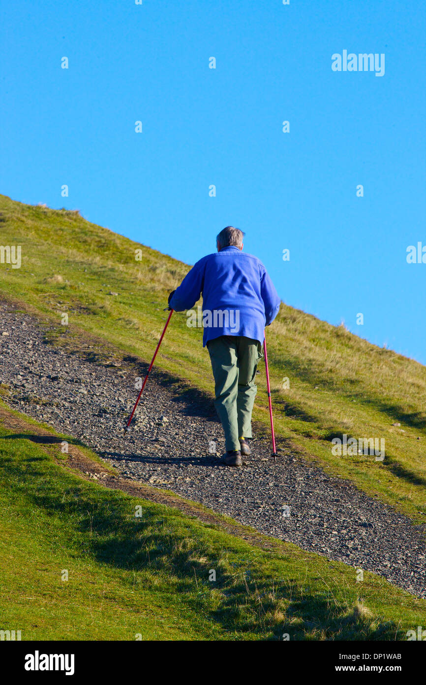 Elderly walker ascending hill by a path with walking poles. Stock Photo