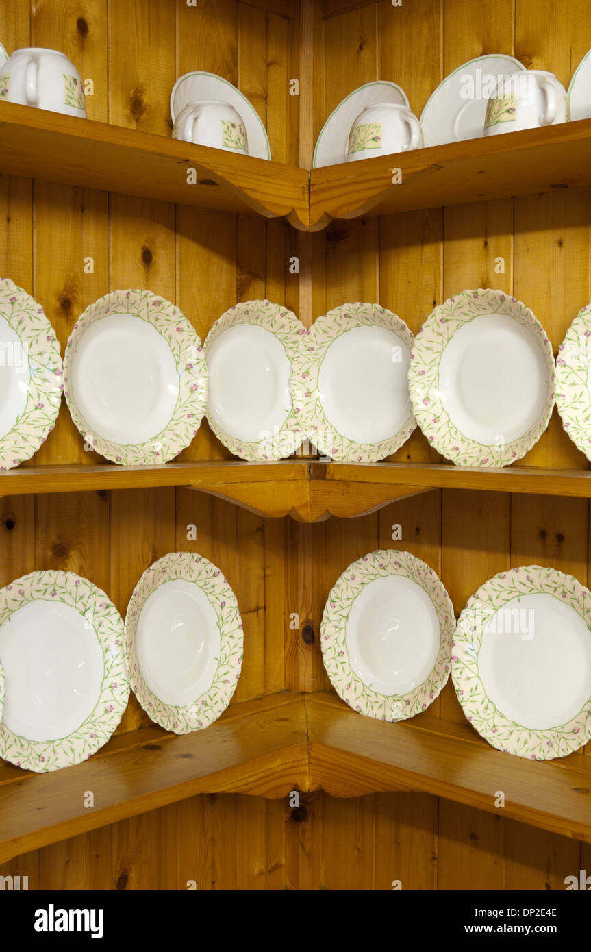 Plates stood on edge on corner shelves in a country kitchen. Stock Photo