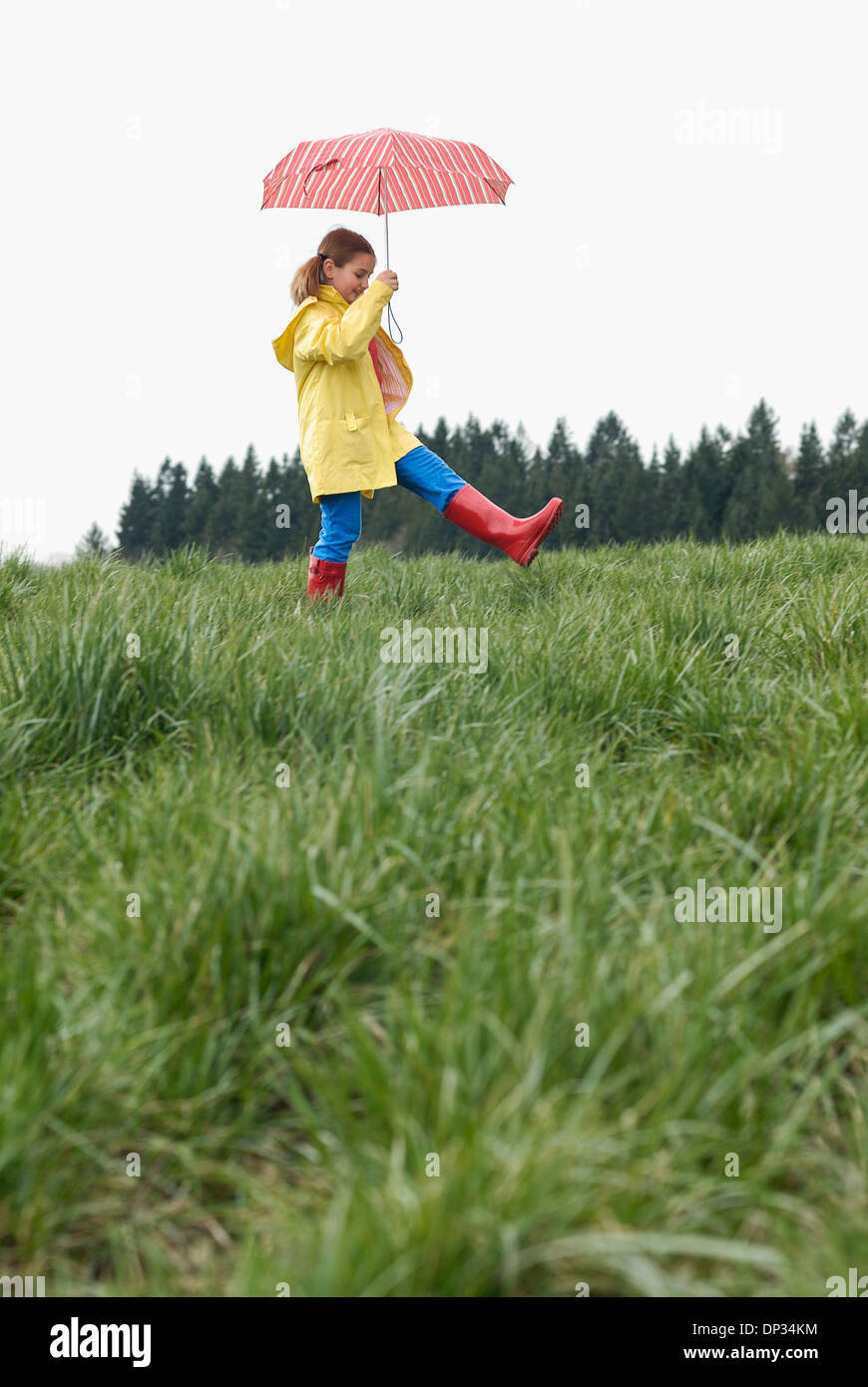 A young girl holding a red umbrella and wearing red rubber boots Stock Photo