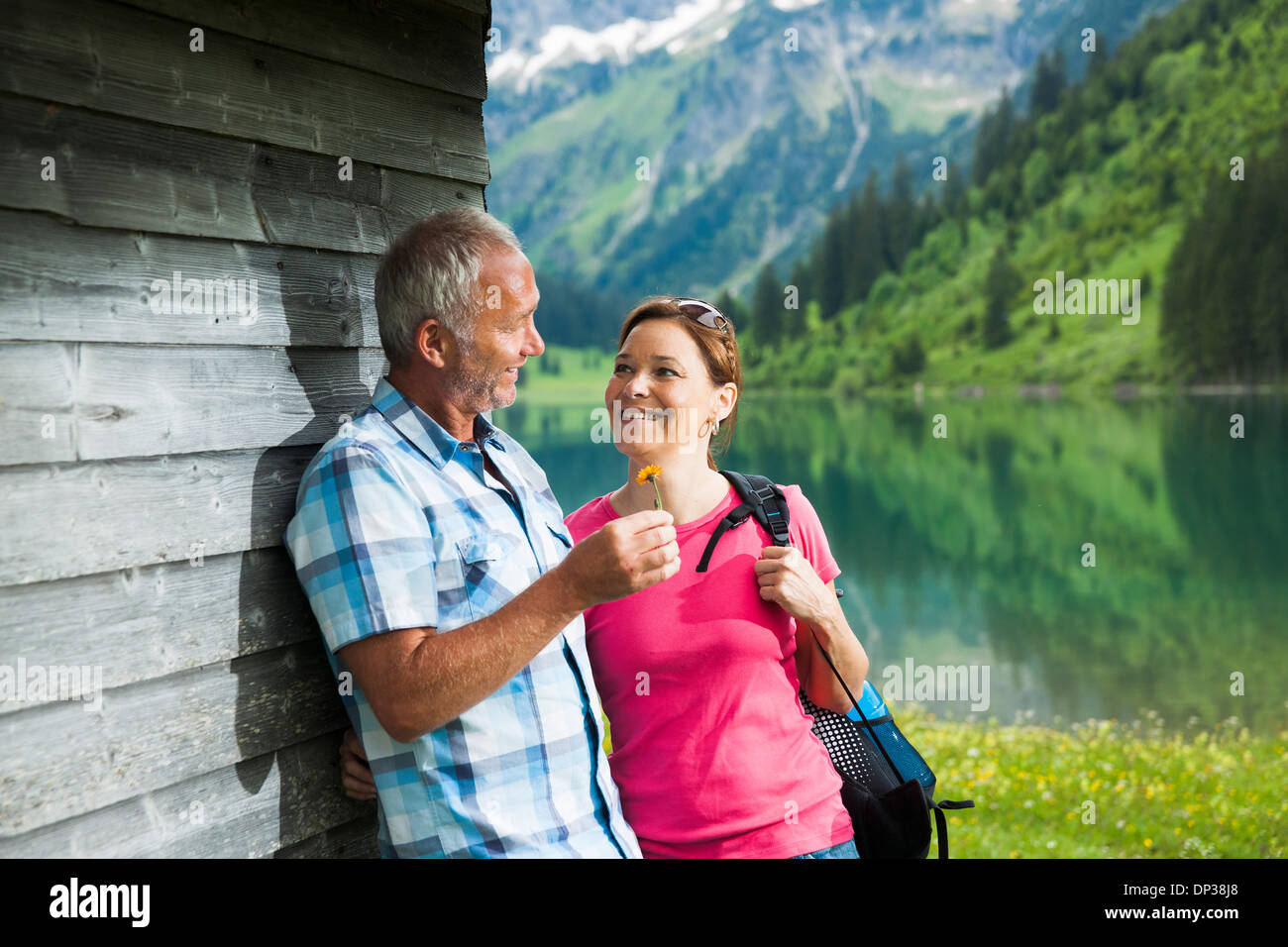 Mature man offering flower to mature woman, standing next to building at Lake Vilsalpsee, Tannheim Valley, Austria Stock Photo