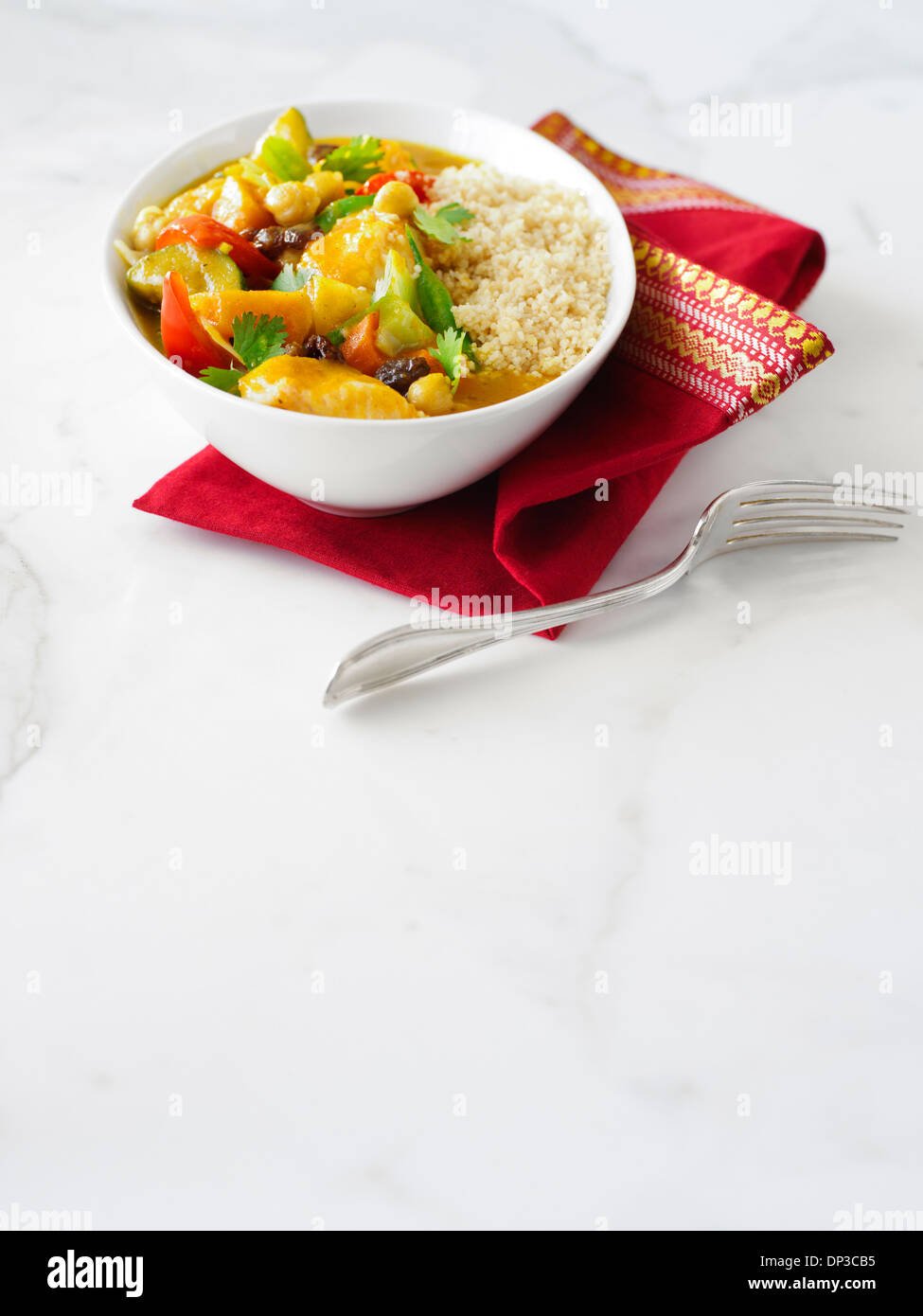 Vegetarian lunch, Bowl of Couscous with Curried Vegetables with red napkin and fork on white