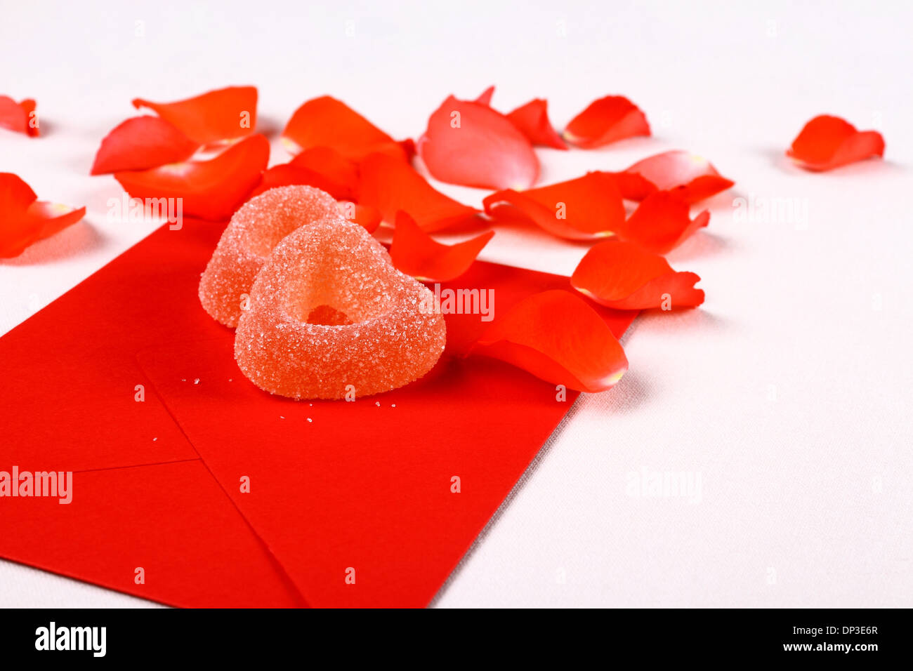 Two hearts from sugar candies on red envelope and petals, close up Stock Photo