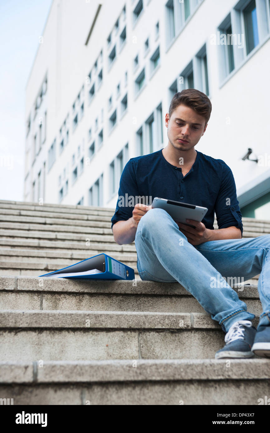 Young man sitting on steps outdoors, using tablet computer, Germany ...