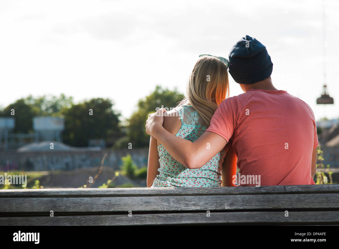 Backview of teenage boy with arm around teenage girl, sitting on bench outdoors, Germany Stock Photo
