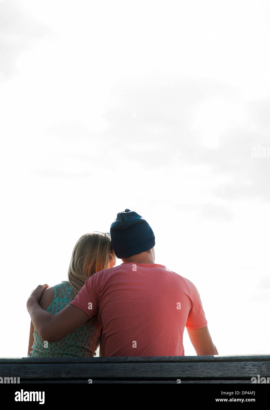 Backview of teenage boy with arm around teenage girl, sitting on bench outdoors, Germany Stock Photo