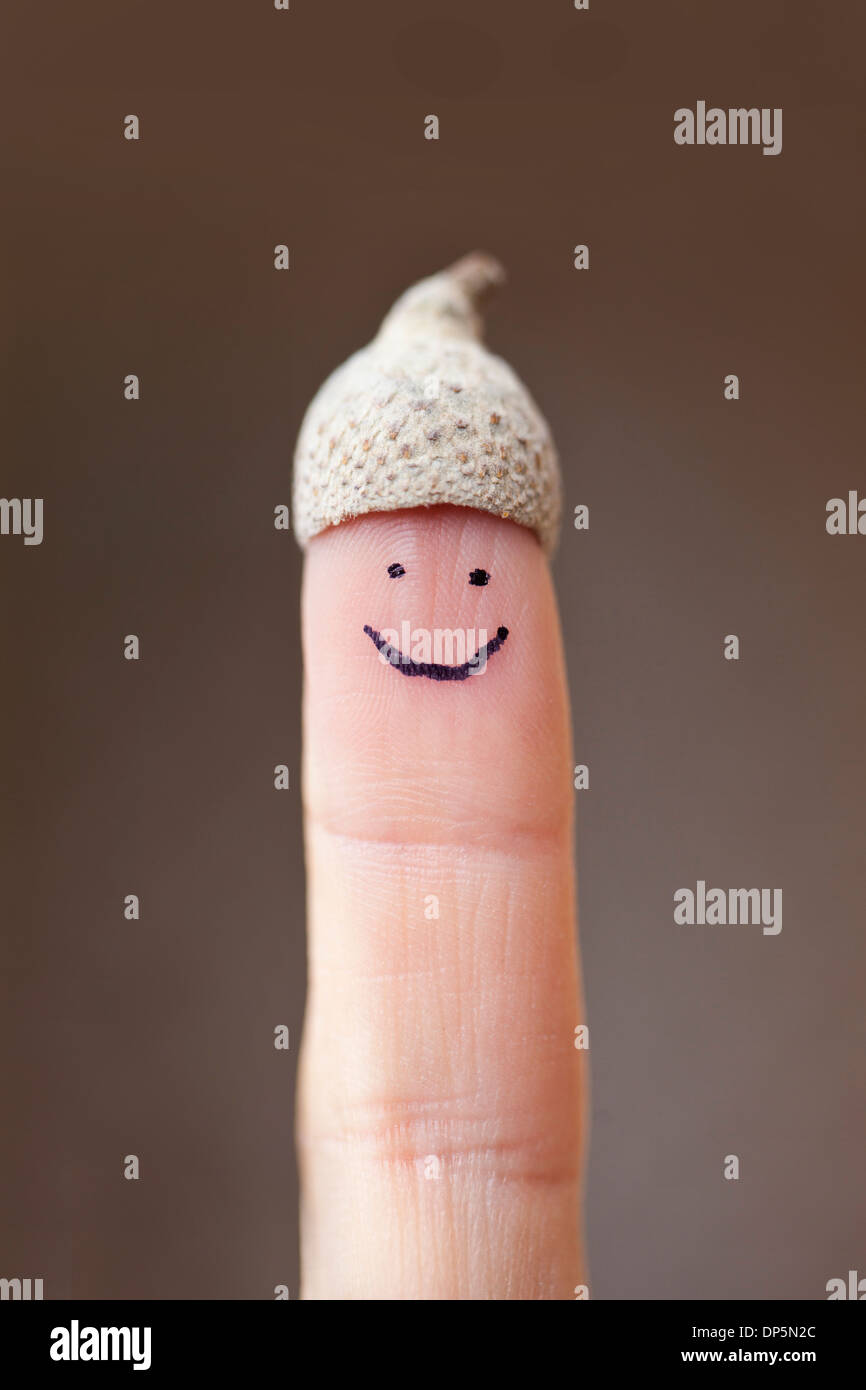 Smiling face painted on a human finger with an acorn shell as a hat. Stock Photo
