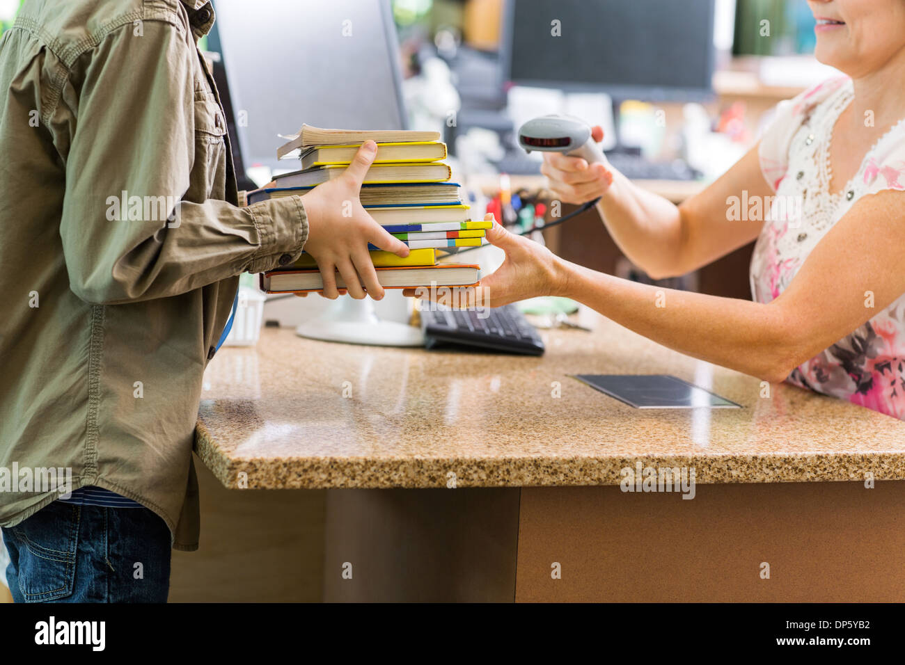 Schoolboy Holding Books At Library Counter Stock Photo