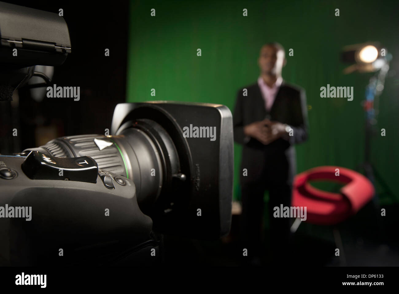 Foreground television camera zoom lens with a presenter out-of-focus in the background. Stock Photo