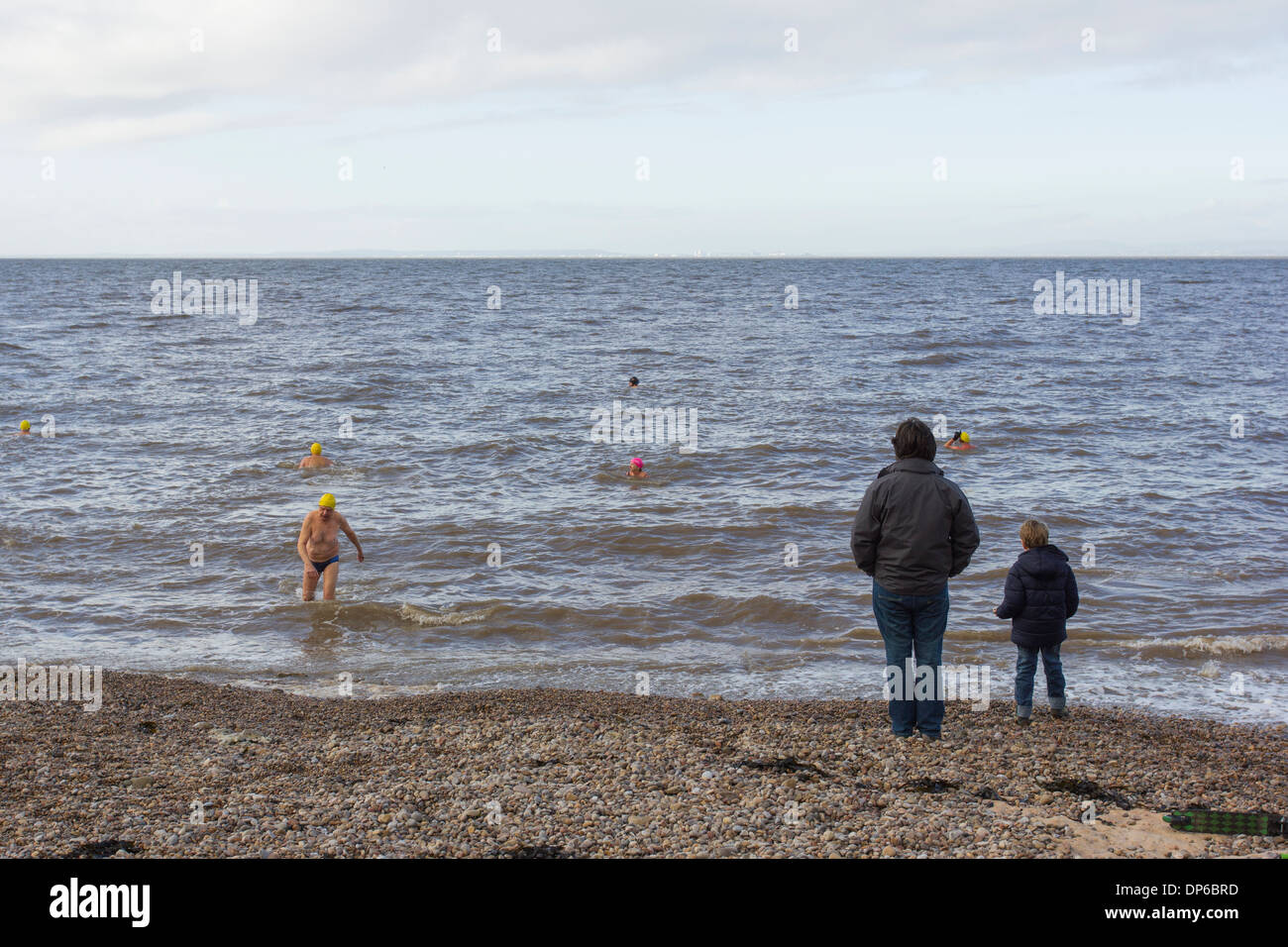 Man and boy watching people swimming in the sea in winter Stock Photo