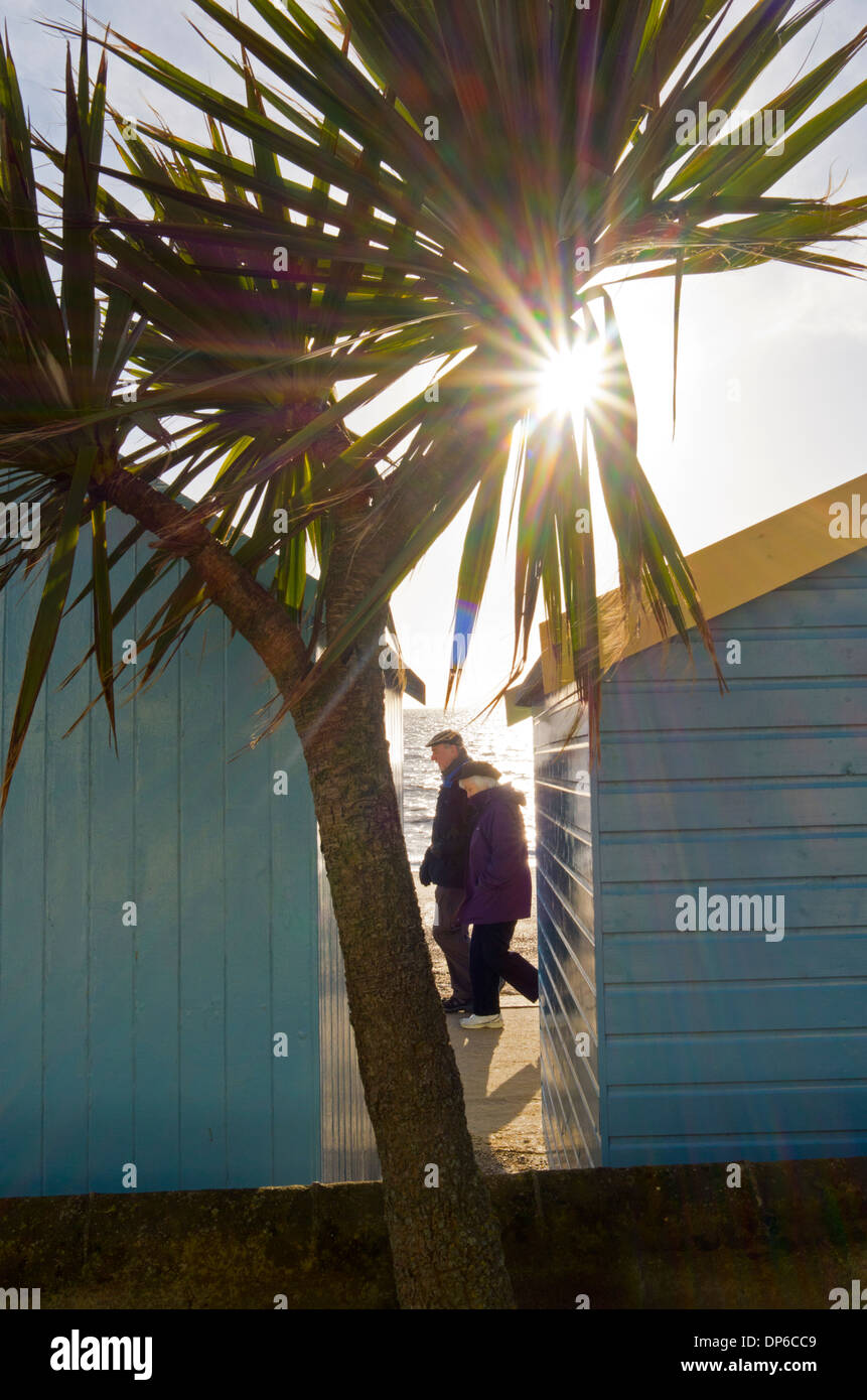 Elderly couple walking along seafront promenade, caught between two beach huts. Stock Photo