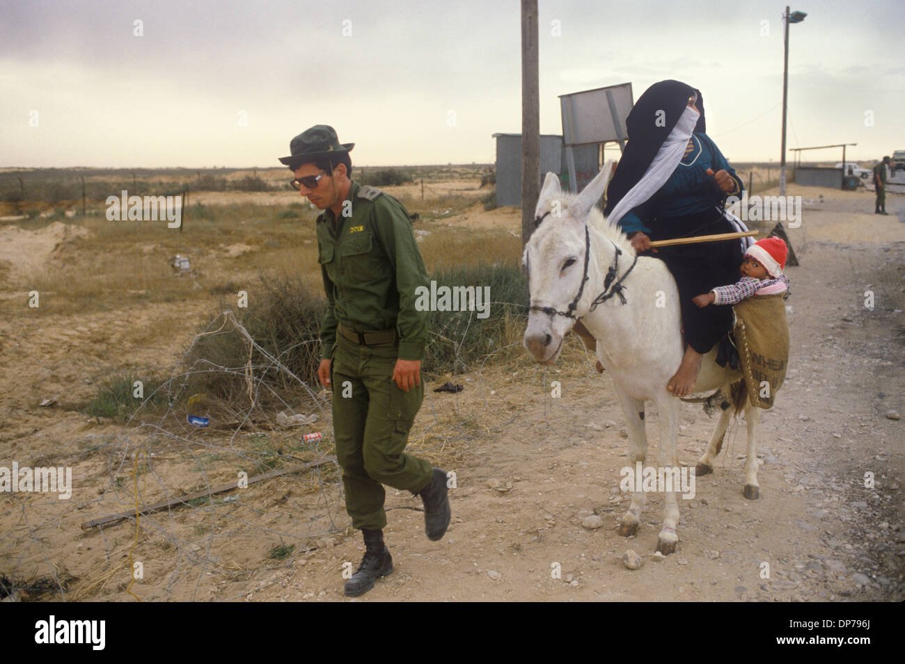 Rafah Crossing 1980s. Bedouin woman with child riding a donkey and Israeli soldier at the new crossing she is being led through by an Israeli soldier.  When Israel withdrew from the Sinai in 1982, Rafah was split into a Gazan part and an Egyptian part, dividing families, separated by barbed-wire barriers. The core of the city was destroyed by Israel and Egypt to create a large buffer zone. Rafah, Palestinian, Gaza Strip April 1982. HOMER SYKES Stock Photo