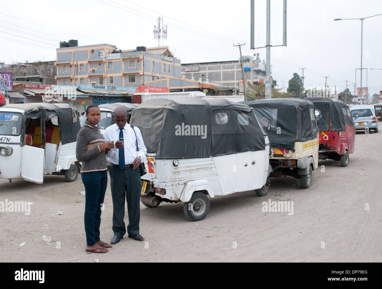 Young African couple using mobile phone near Tuk Tuk taxis at Kaijado on Nairobi Namanga Road Kenya Africa Stock Photo