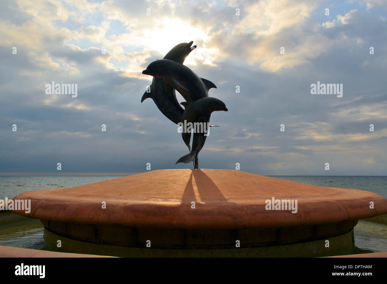 statue of couple jumping dolphins, blue sea and sky, clouds, sun Stock Photo