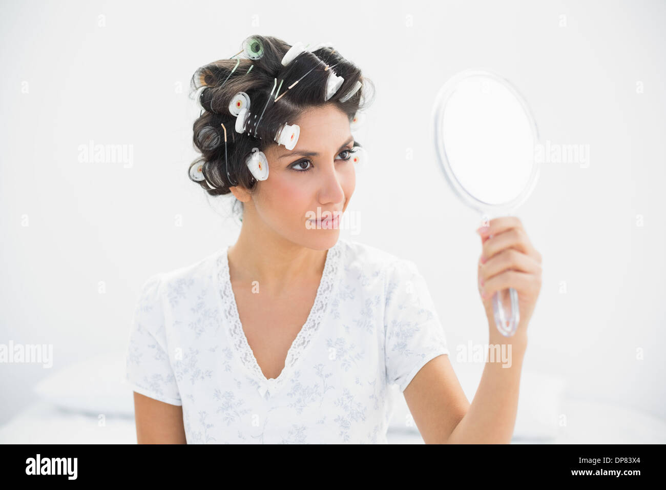 Happy brunette in hair rollers holding hand mirror Stock Photo