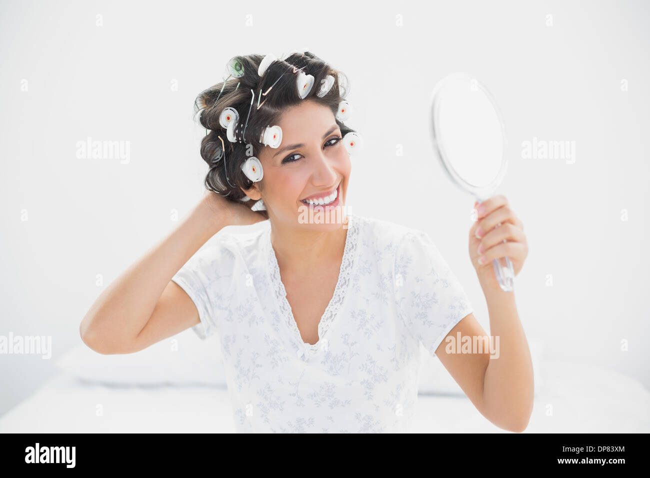 Smiling brunette in hair rollers holding hand mirror Stock Photo