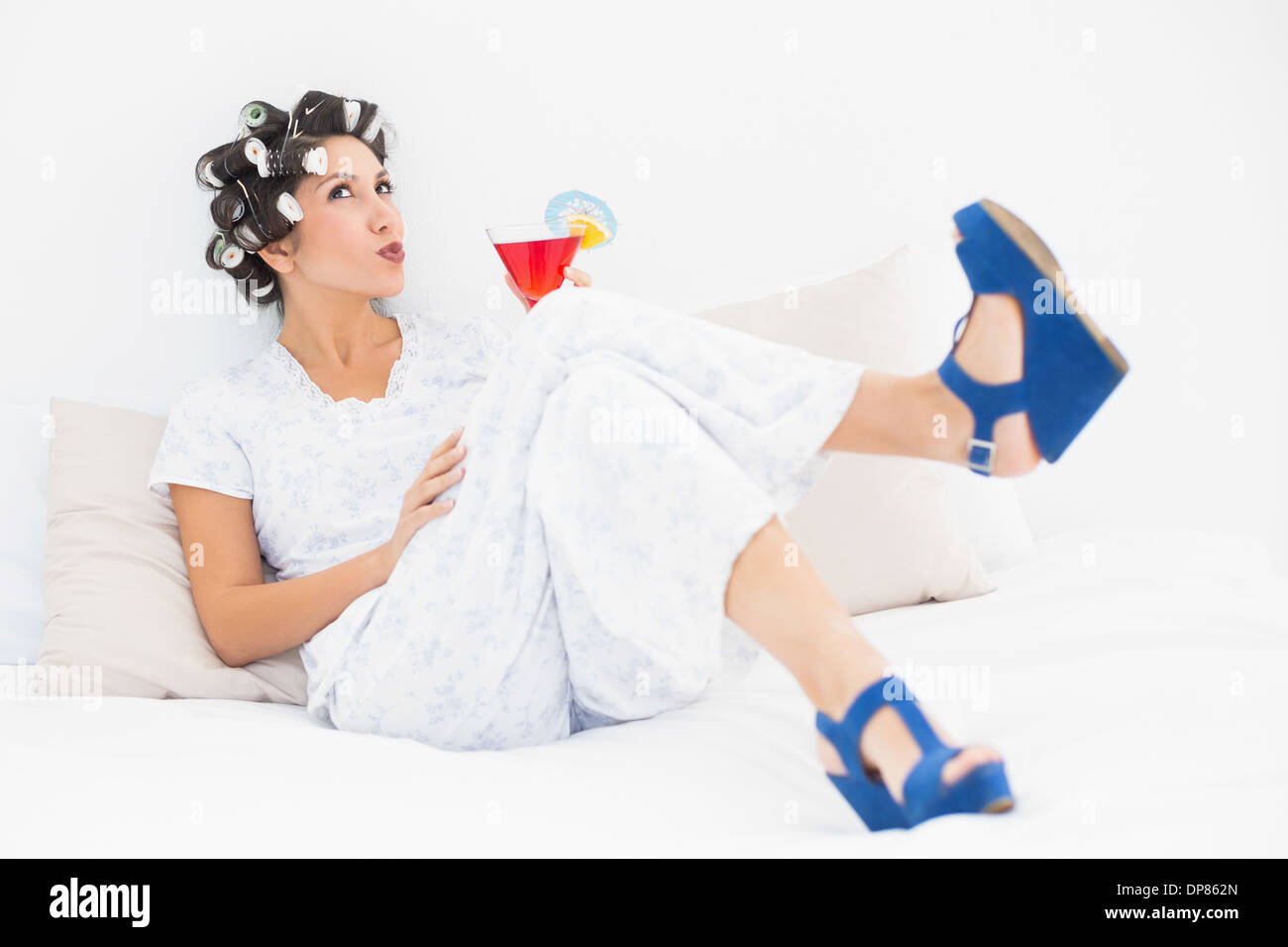 Brunette in hair curlers and wedge shoes having a cocktail Stock Photo