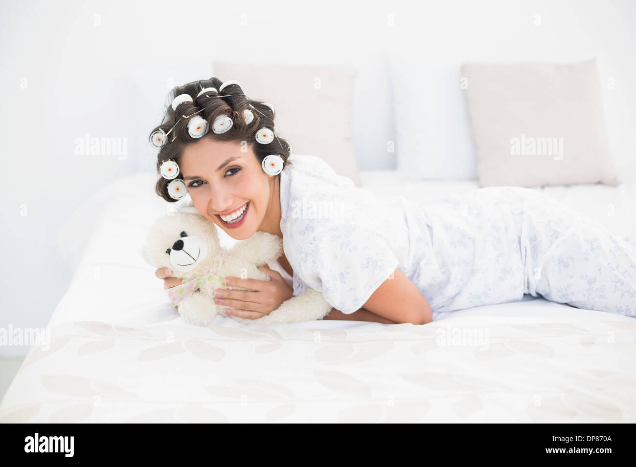 Pretty brunette in hair rollers cuddling her teddy on bed Stock Photo