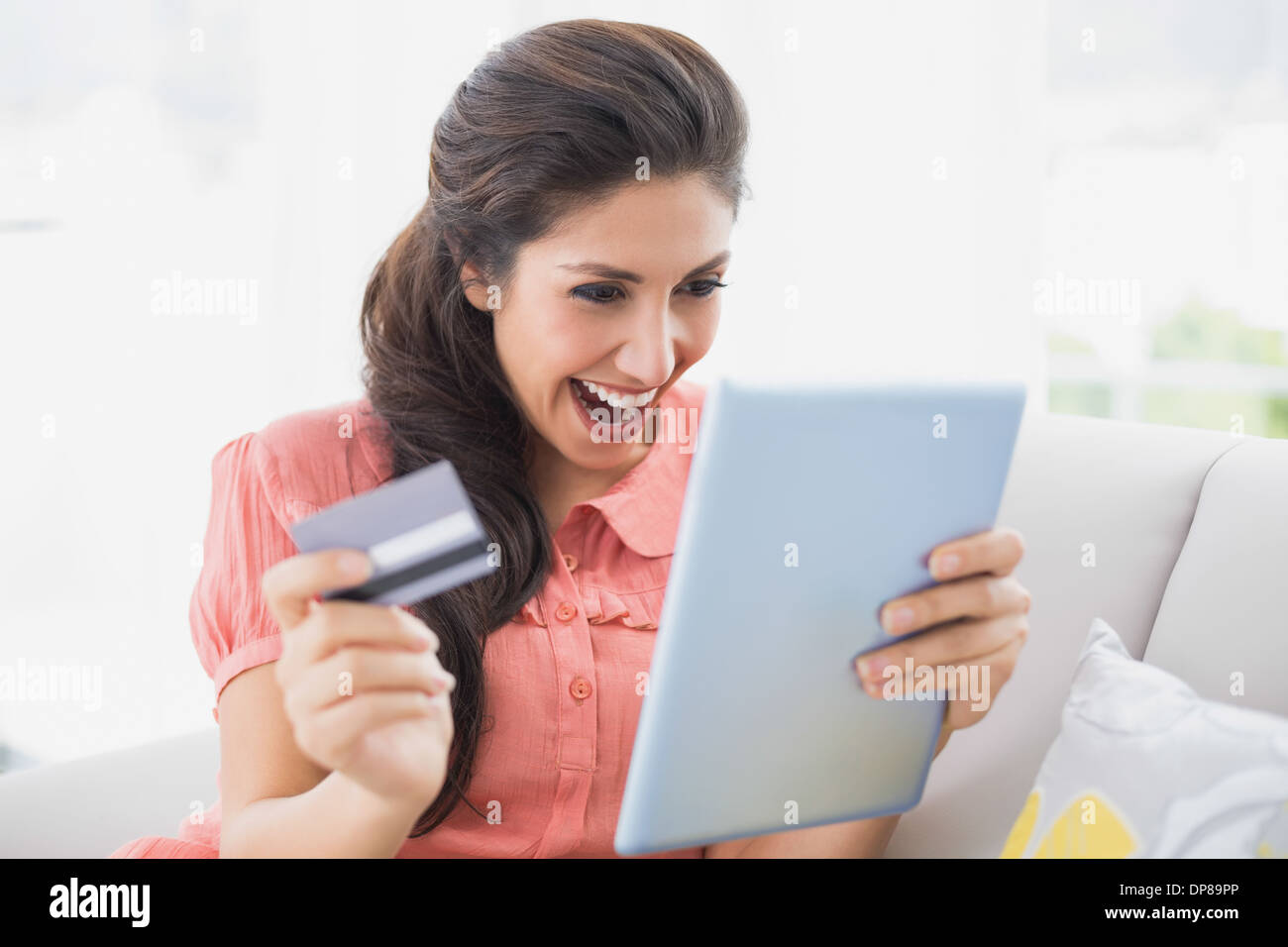 Ecstatic brunette sitting on her sofa using tablet to shop online Stock Photo