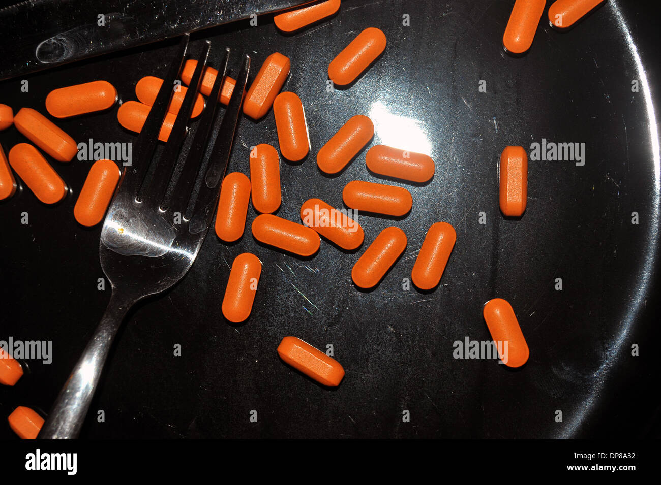 A black dinner plate covered in bright orange pills. Stock Photo