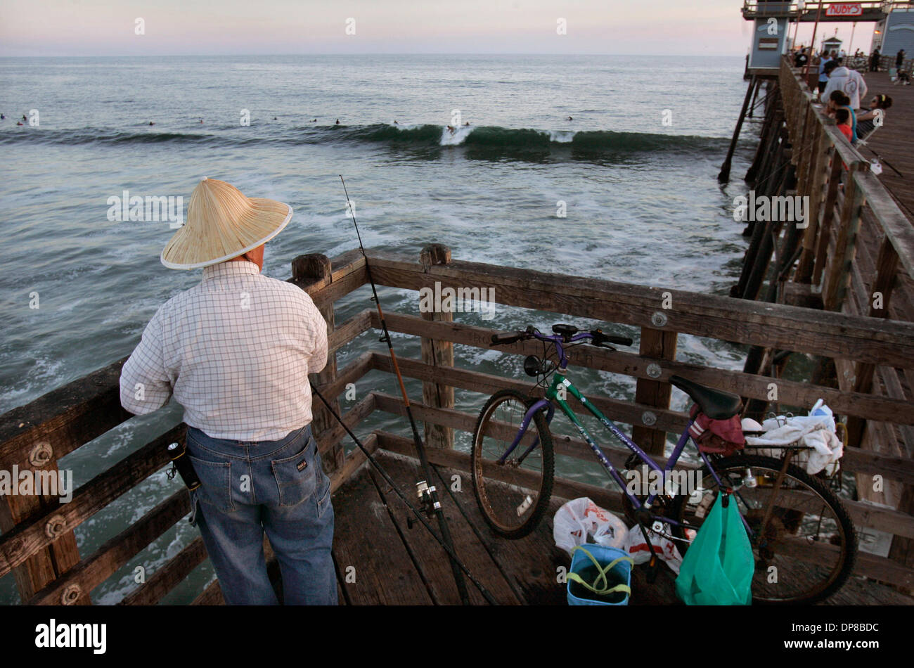 (Published 10/8/2006, B-7:CO,C)  June 1, 2006, Oceanside, California, USA A man named LIN (cq) fishes from the south side of the Oceanside Pier in the evening as a a surfer takes off on a wave nearby Mandatory Credit: photo by Charlie Neuman/San Diego Union-Tribune/Zuma Press. copyright 2006 San Diego Union-Tribune Stock Photo