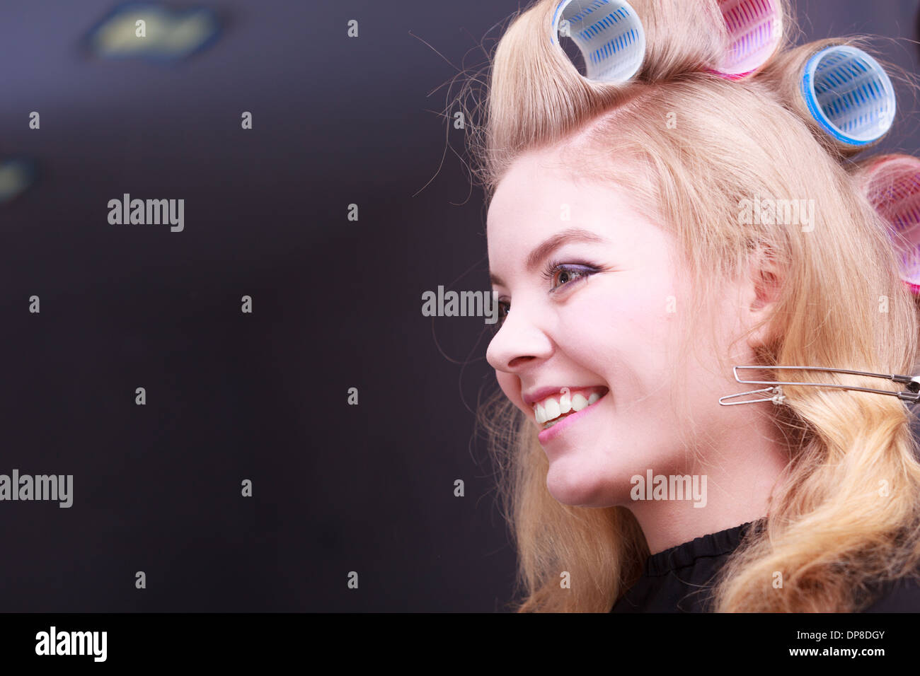 Beautiful young woman in beauty salon. Happy blond girl with hair curlers rollers by hairdresser. Hairstyle. Stock Photo