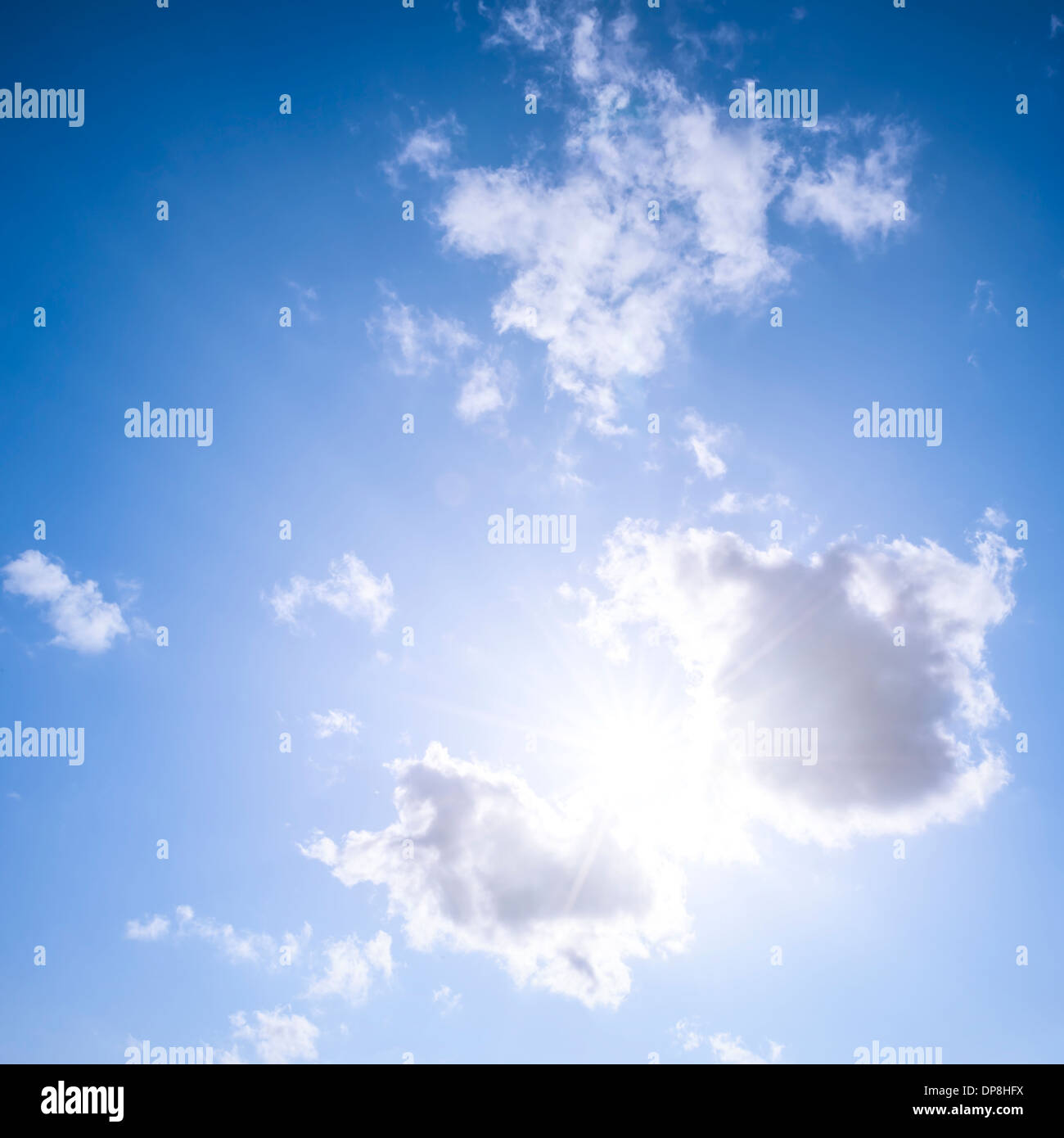 Square blue sky background with bright sun flare shining through clouds Stock Photo