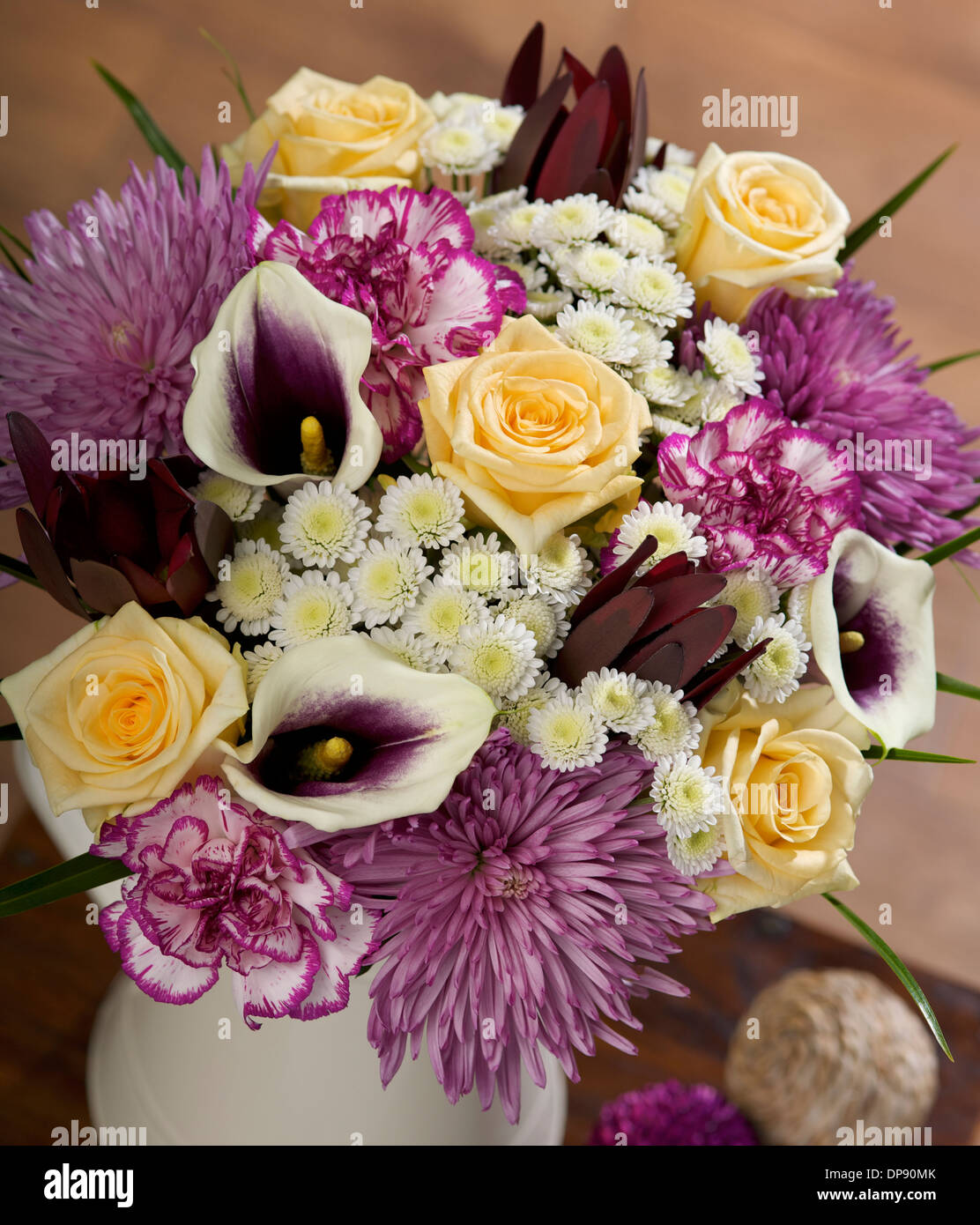 white Stallion Chrysanthemums, purple edged spray Carnations, maroon Leucadendron, purple Calla Lilies and Avalanche Roses in a vase in a home setting Stock Photo