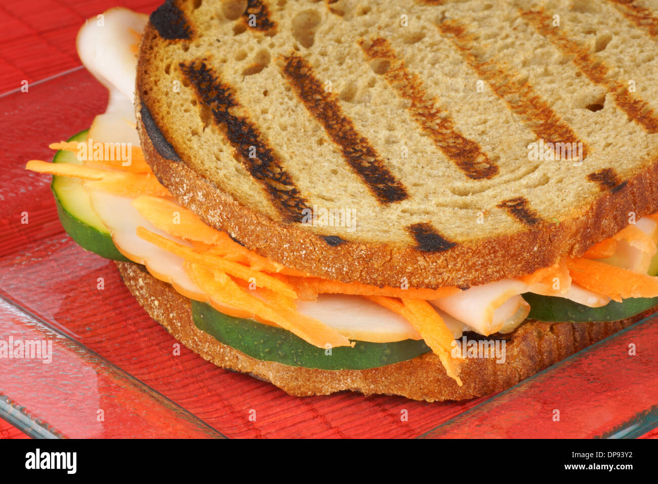 Close-up of a roasted turkey sandwich with julienne carrots and slices of cucumber on a transparent glass plate. Stock Photo