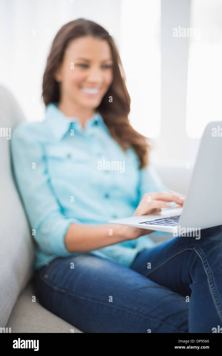 Smiling gorgeous brunette sitting on sofa using laptop Stock Photo
