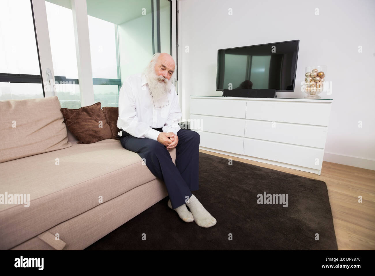 Sad senior man sitting on sofa in living room Stock Photo