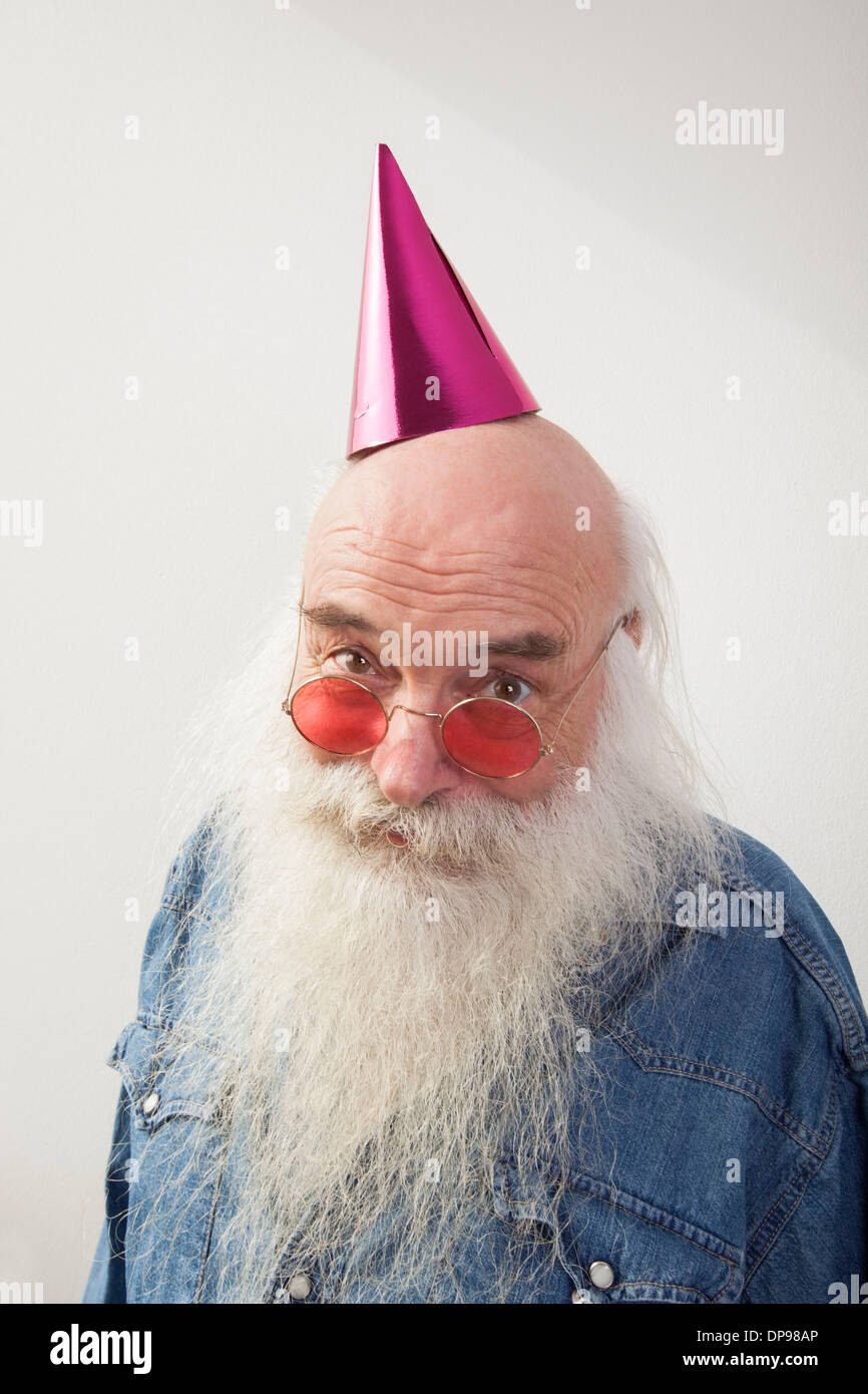 Portrait of senior man wearing red glasses and party hat against gray background Stock Photo