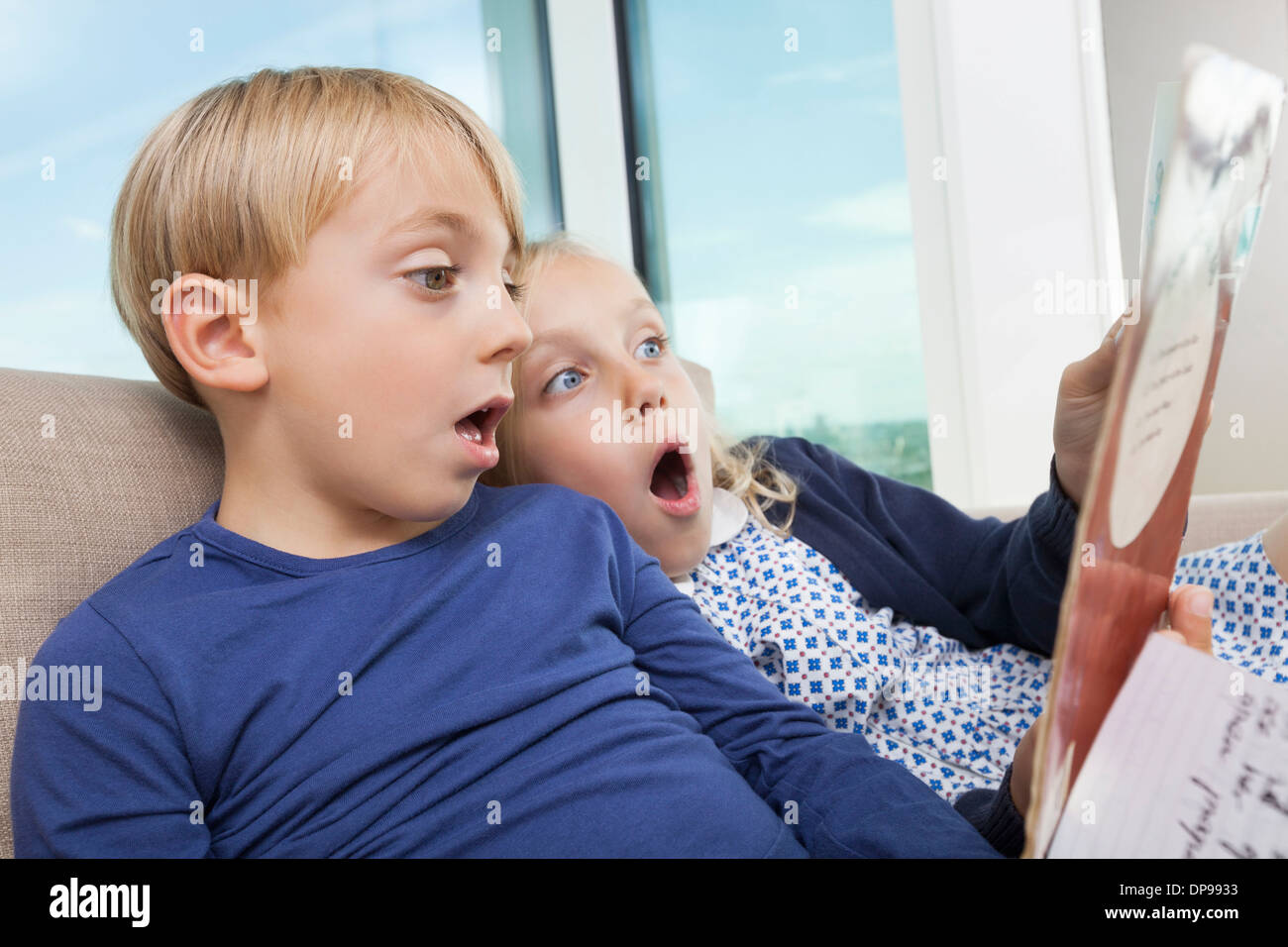 Shocked brother and sister reading storybook at home Stock Photo