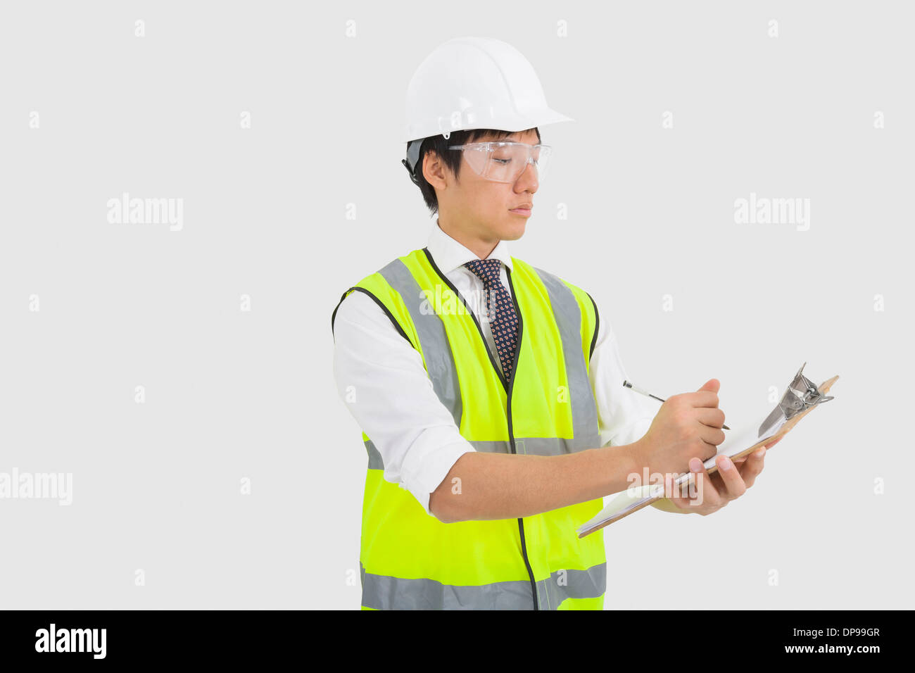 Man in reflector vest and hard hat writing on clipboard in office Stock Photo