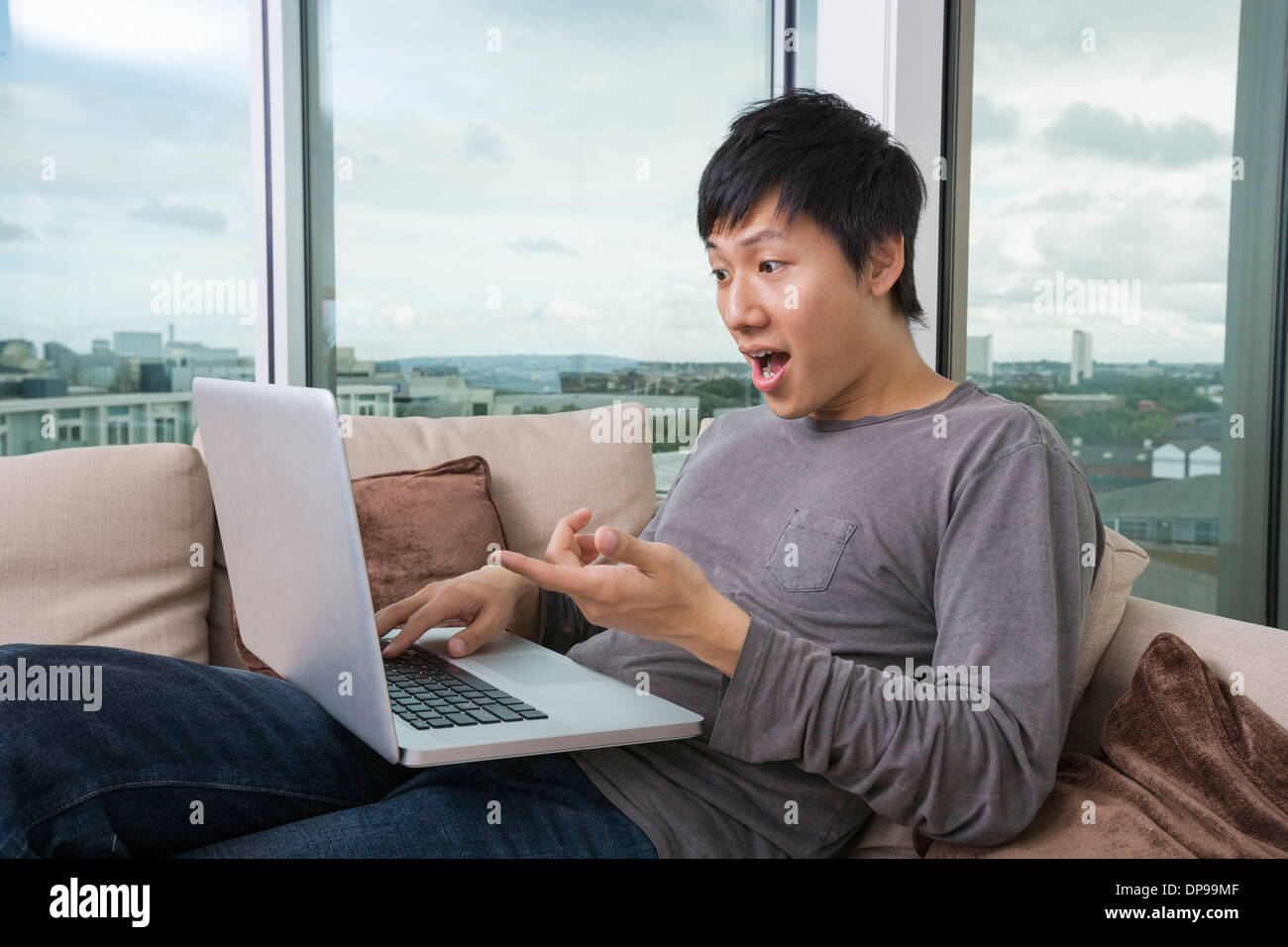 Shocked man using laptop on sofa at home Stock Photo