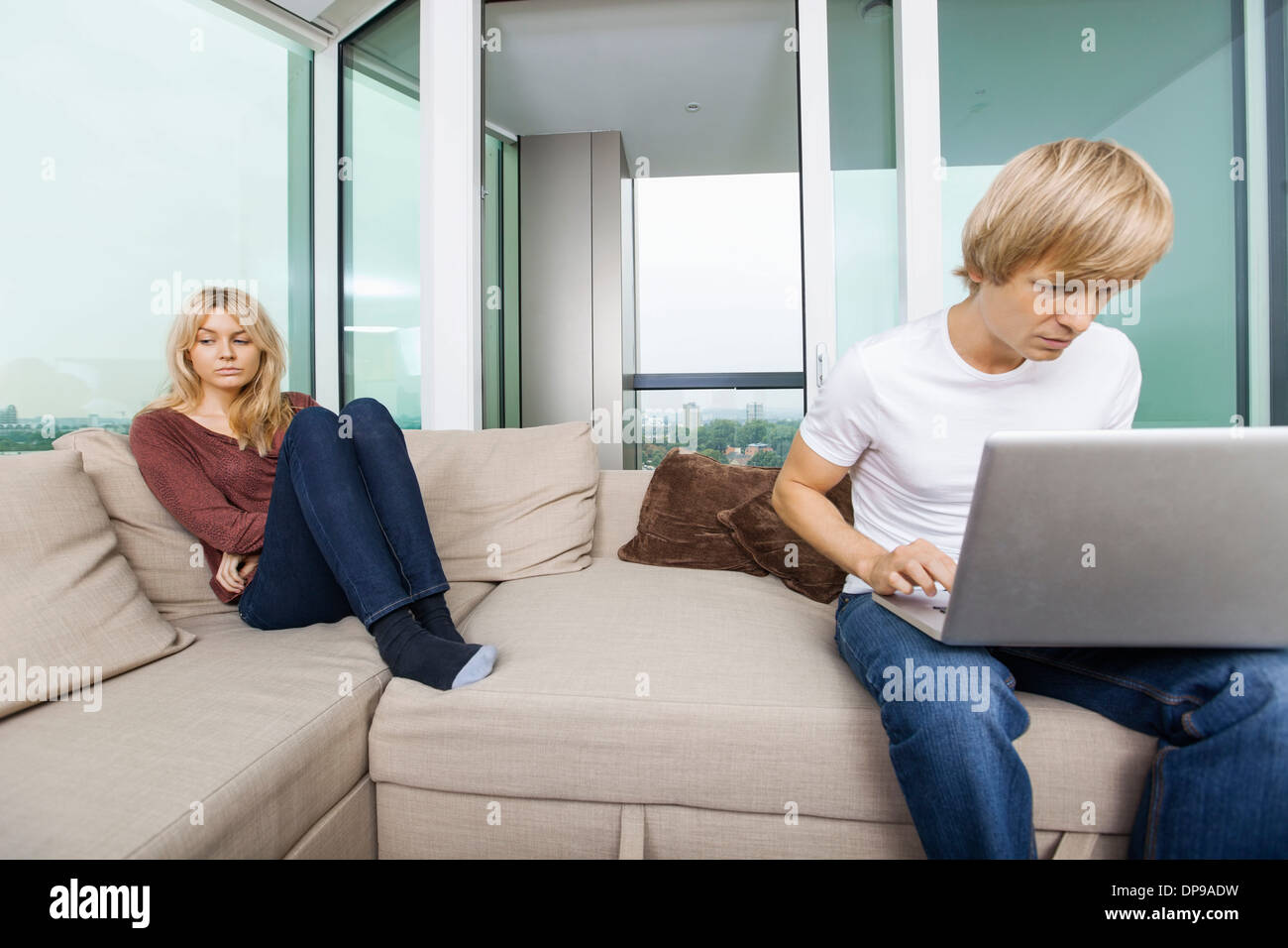 Sad woman beside man using laptop in living room at home Stock Photo